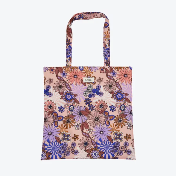 Le sac tote bag est de format carré, avec des anses, il est de couleur nude, rose poudré en fond avec des motifs floraux violet, mauve, saumon, pêche avec des motifs fleuris lui donnant un petit côté vintage année 70. Le tissu est imperméable impression en Europe, et dessiné en France par une illustratrice basée en France Stéphanie Piogé