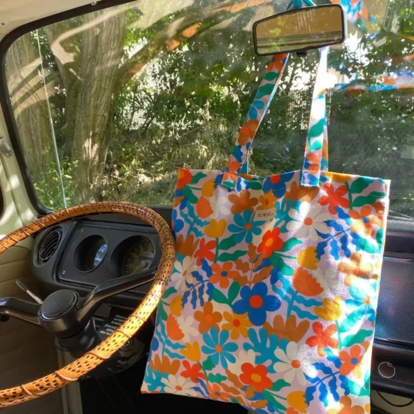 Sac tote bag Elness.co avec son motif fleuri et vintage en coton certifié oeko tex. Il a un look très année 70 vintage, il est multicolore bleu turquois blanc vert jaune orange rose. Il est fabriqué en France plus précisément en Charente près d'Angoulême. Un sac dans un combi volswagen années 70.