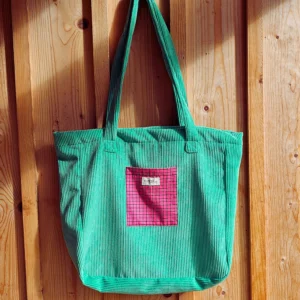 Le grand sac shopping, idéal pour aller en cours au travail, en shopping. Le sac est en velour vert pelouse, vert flashy avec une poche quadirllé rose et noir et tout l'intérieur est également dans ce même colori rose fushia. Il est fabriqué en France la fabrication est locale en Charente dans un atelier d'insertion