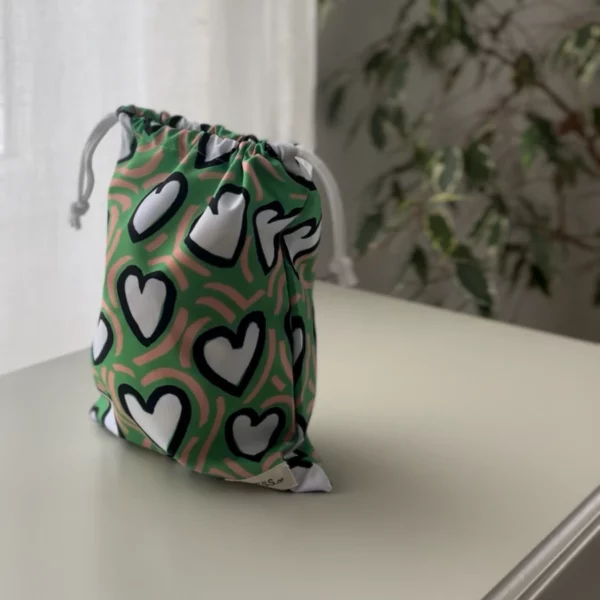 Pochette imperméable et écoresponsable, confectionnée à partir de chutes de tissus et fermée par des liens en coton recyclé, idéale pour transporter maillot mouillé, produits de beauté ou linge sale en voyage.