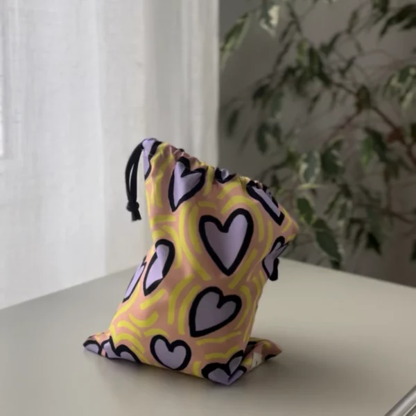Pochette imperméable et écoresponsable, confectionnée à partir de chutes de tissus et fermée par des liens en coton recyclé, idéale pour transporter maillot mouillé, produits de beauté ou linge sale en voyage.