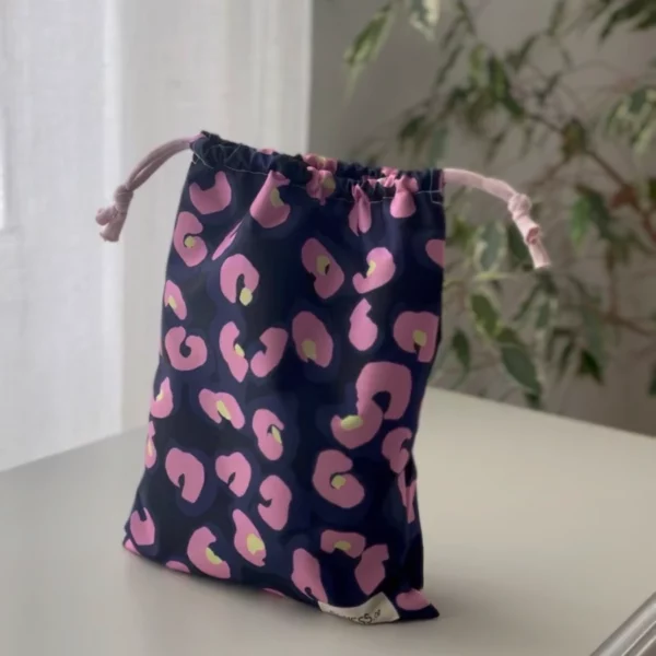 Pochette imperméable et écoresponsable, confectionnée à partir de chutes de tissus et fermée par des liens en coton recyclé, idéale pour transporter maillot mouillé, produits de beauté ou linge sale en voyage.